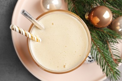 Glass of delicious eggnog and decorated fir branch on gray table, flat lay