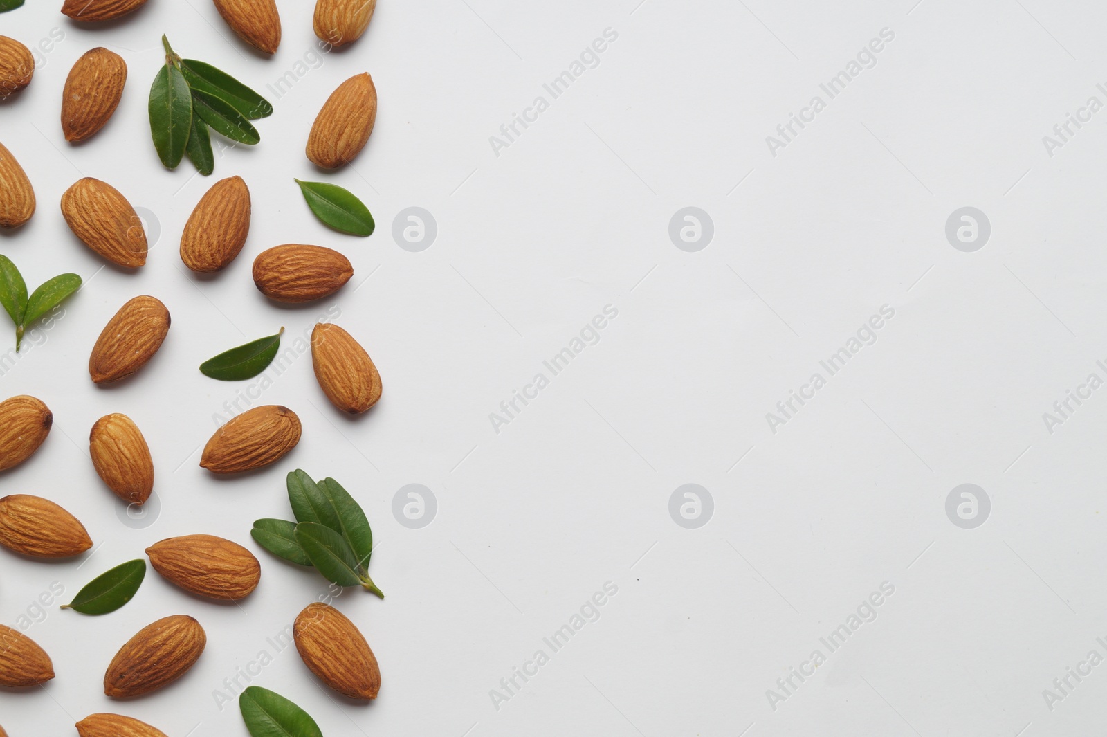 Photo of Delicious almonds and fresh leaves on white background, flat lay. Space for text