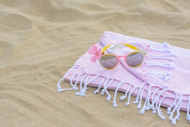 Blanket with stylish sunglasses and flower on sand outdoors, space for text. Beach accessories