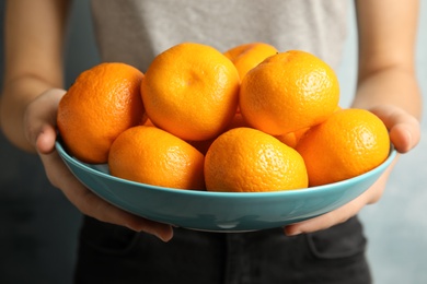 Photo of Woman holding bowl of ripe tangerines, closeup