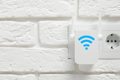 Image of New modern repeater with Wi-Fi symbol plugged into socket on white brick wall, space for text