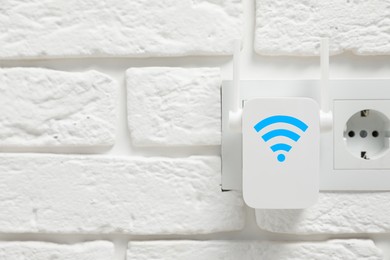 New modern repeater with Wi-Fi symbol plugged into socket on white brick wall, space for text