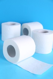 Photo of Soft toilet paper rolls on light blue background, closeup