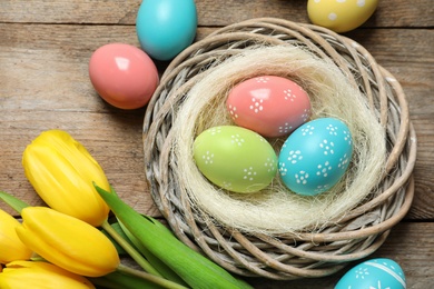 Flat lay composition of wicker nest with painted Easter eggs and tulips on wooden table