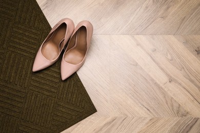 Photo of Stylish door mat and shoes on wooden floor, top view. Space for text