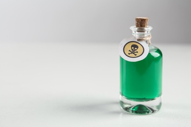 Photo of Glass bottle of poison with warning sign on light background. Space for text