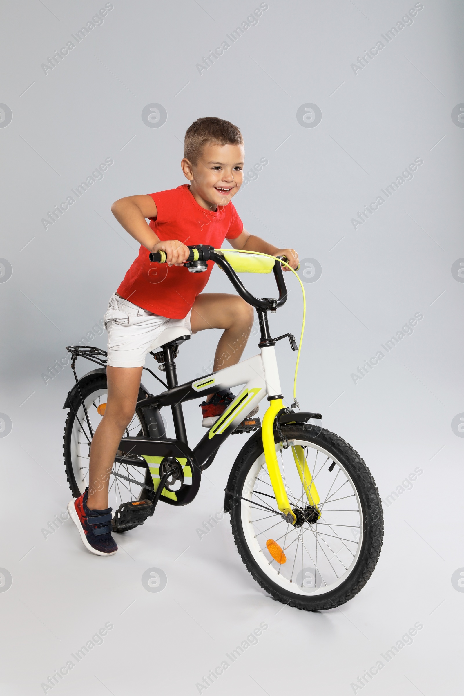Photo of Cute little boy riding bicycle on grey background