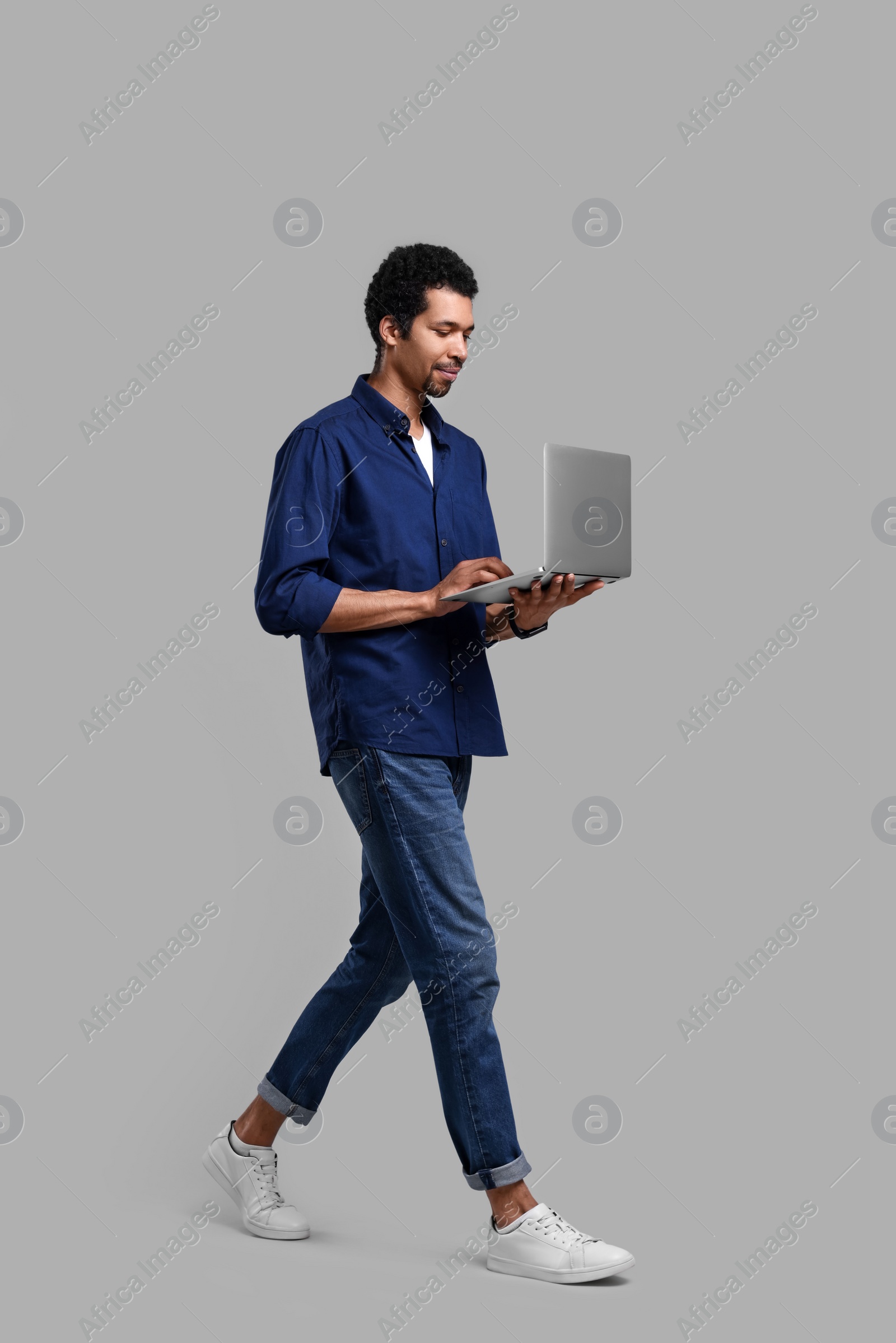 Photo of Handsome man using laptop while walking on grey background