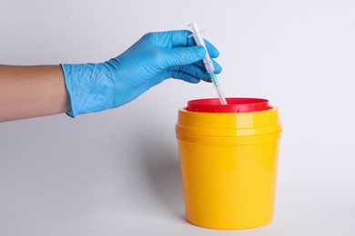 Doctor throwing used syringe into sharps container on white background, closeup