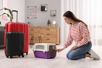 Photo of Woman preparing to travel with dog indoors. Suitcases and pet carrier around her