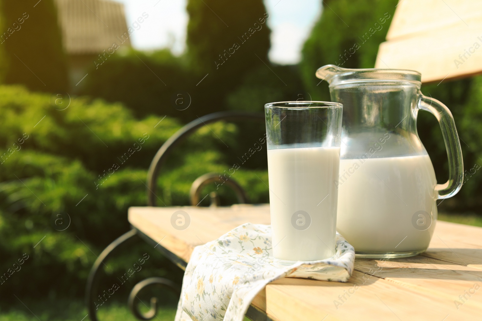 Photo of Jug and glass of tasty fresh milk on wooden bench outdoors, space for text