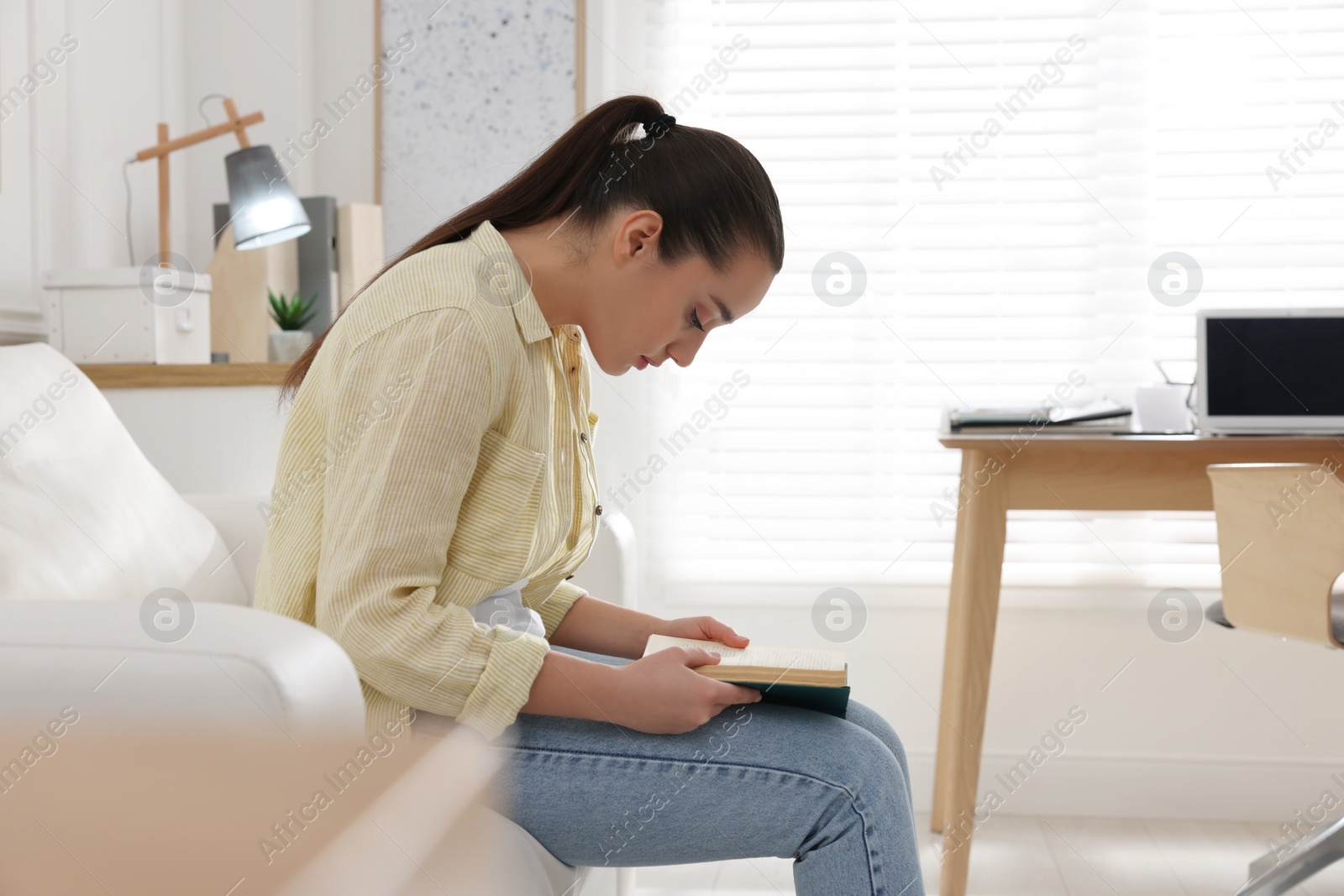 Photo of Young woman with poor posture reading book at home