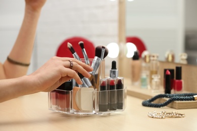 Woman reaching for organizer with cosmetic products and makeup accessories on dressing table indoors, closeup