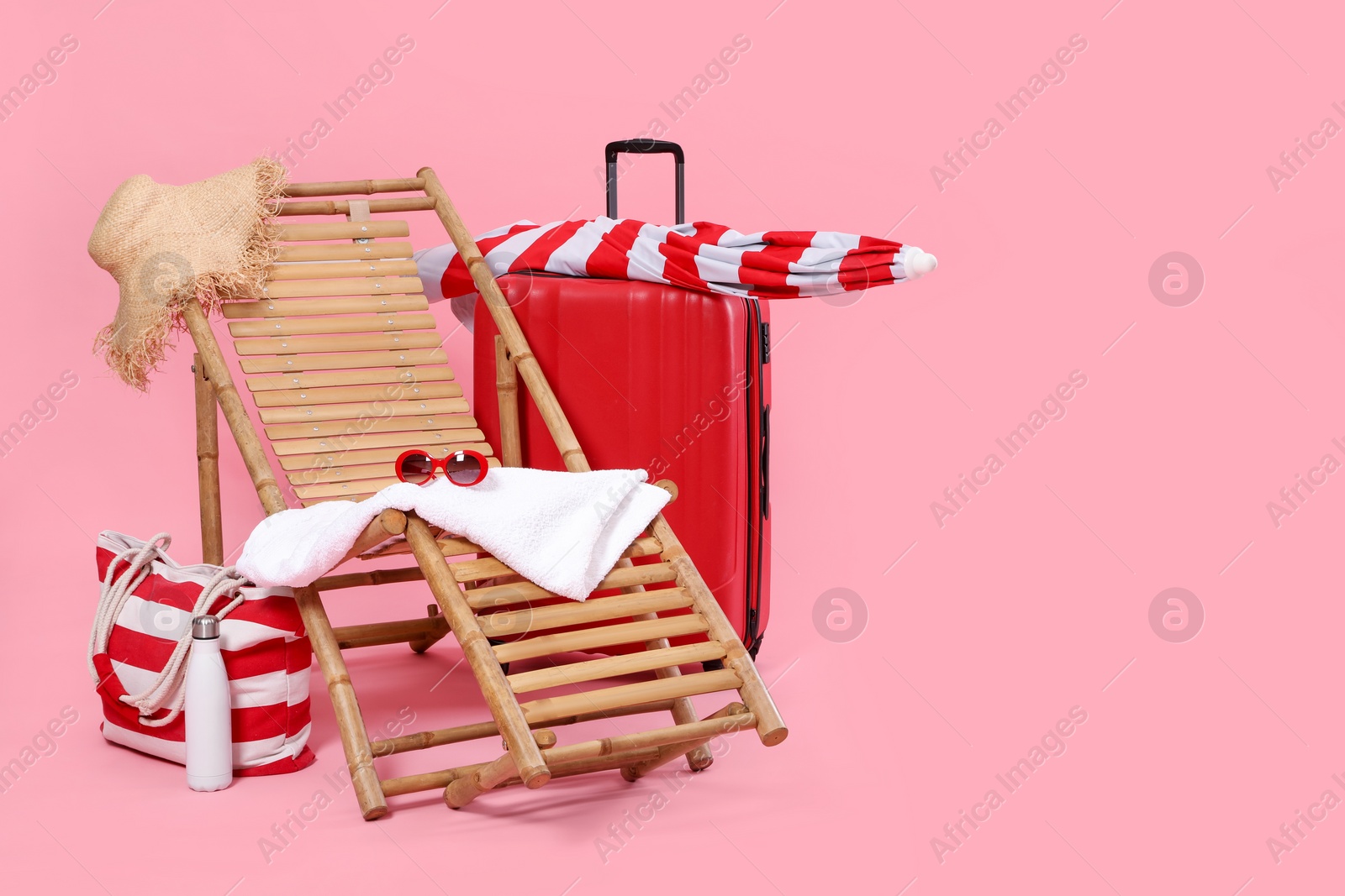 Photo of Deck chair, suitcase and beach accessories on pink background, space for text