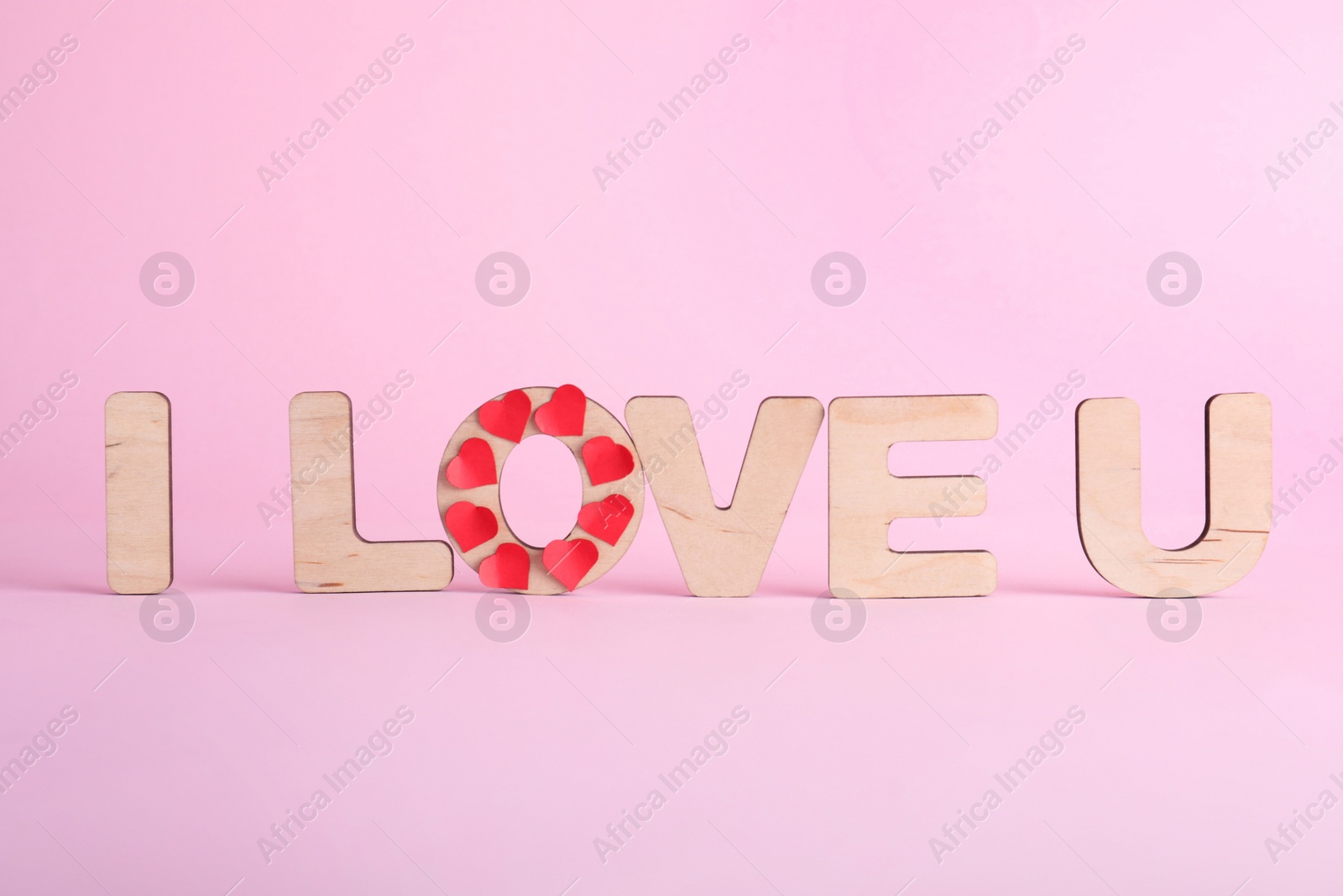 Photo of Phrase I Love You made of wooden letters and red hearts on pink background