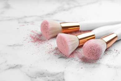 Photo of Different makeup brushes with crushed cosmetic product on white marble table, closeup. Space for text