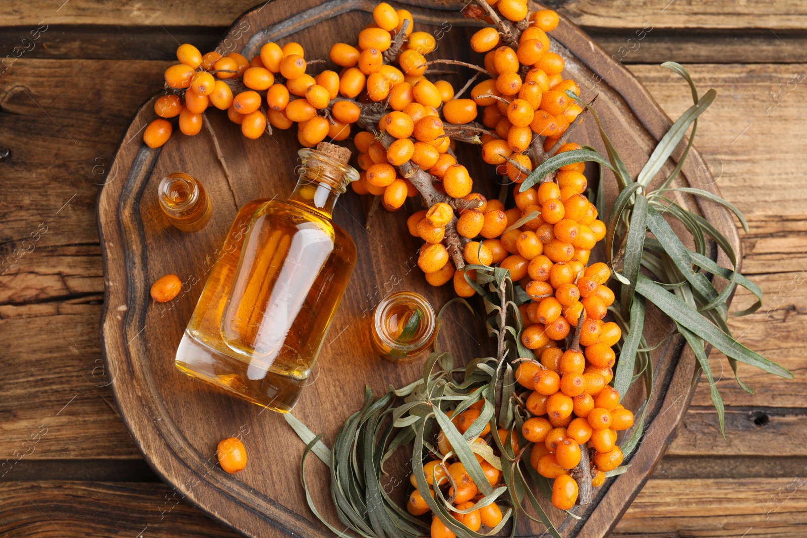 Photo of Natural sea buckthorn oil and fresh berries on wooden table, top view