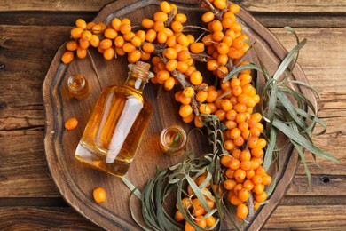 Photo of Natural sea buckthorn oil and fresh berries on wooden table, top view