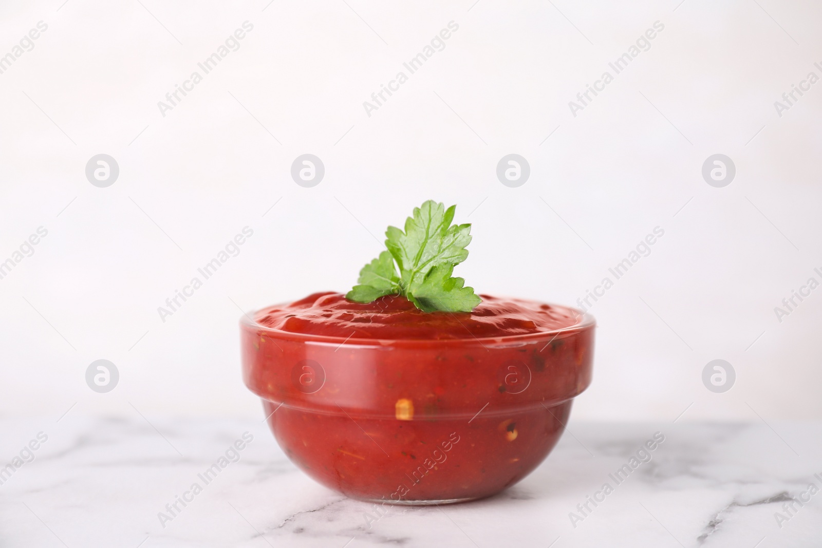 Photo of Bowl of hot chili sauce with parsley on table against white background