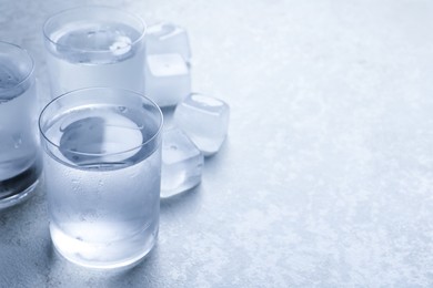 Photo of Shot glasses of vodka with ice on light grey table. Space for text