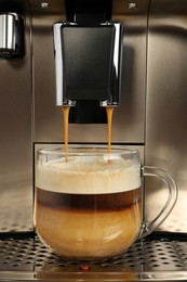 Modern coffee machine making latte into glass cup, closeup