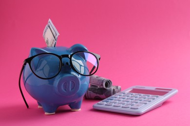 Photo of Financial savings. Piggy bank, dollar banknotes, glasses and calculator on pink background