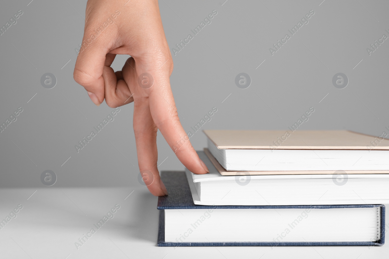 Photo of Woman imitating stepping up on books with her fingers against grey background, closeup