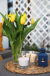 Photo of Burning candles and yellow tulips on rattan garden table outdoors