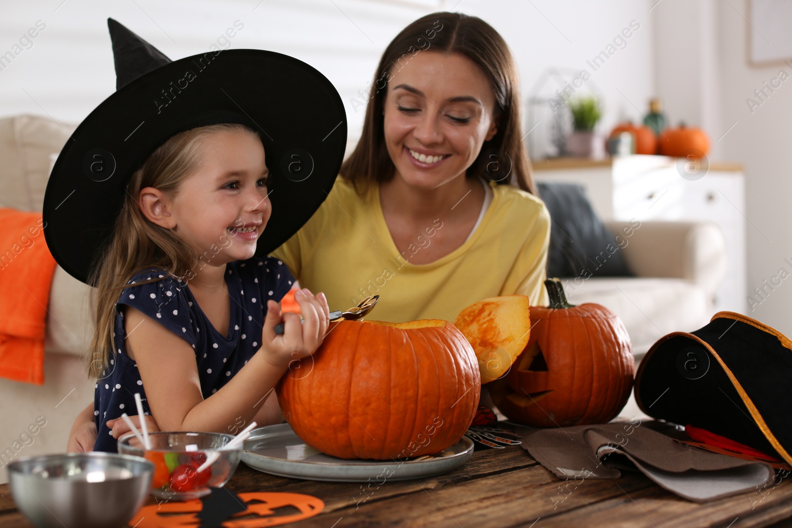 Photo of Mother and daughter making pumpkin jack o'lantern at table indoors. Halloween celebration