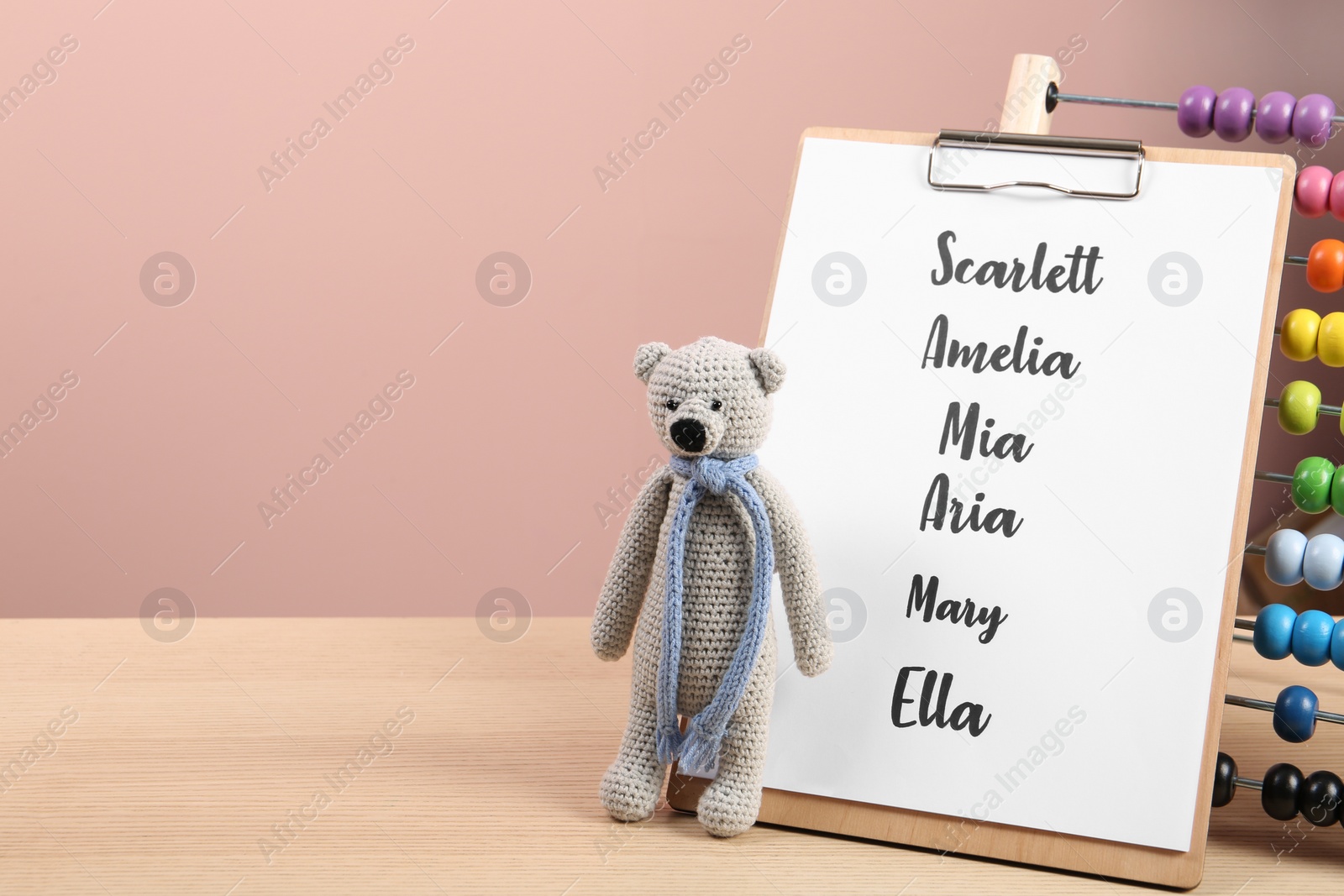 Photo of Clipboard with list of baby names and toys on wooden table. Space for text