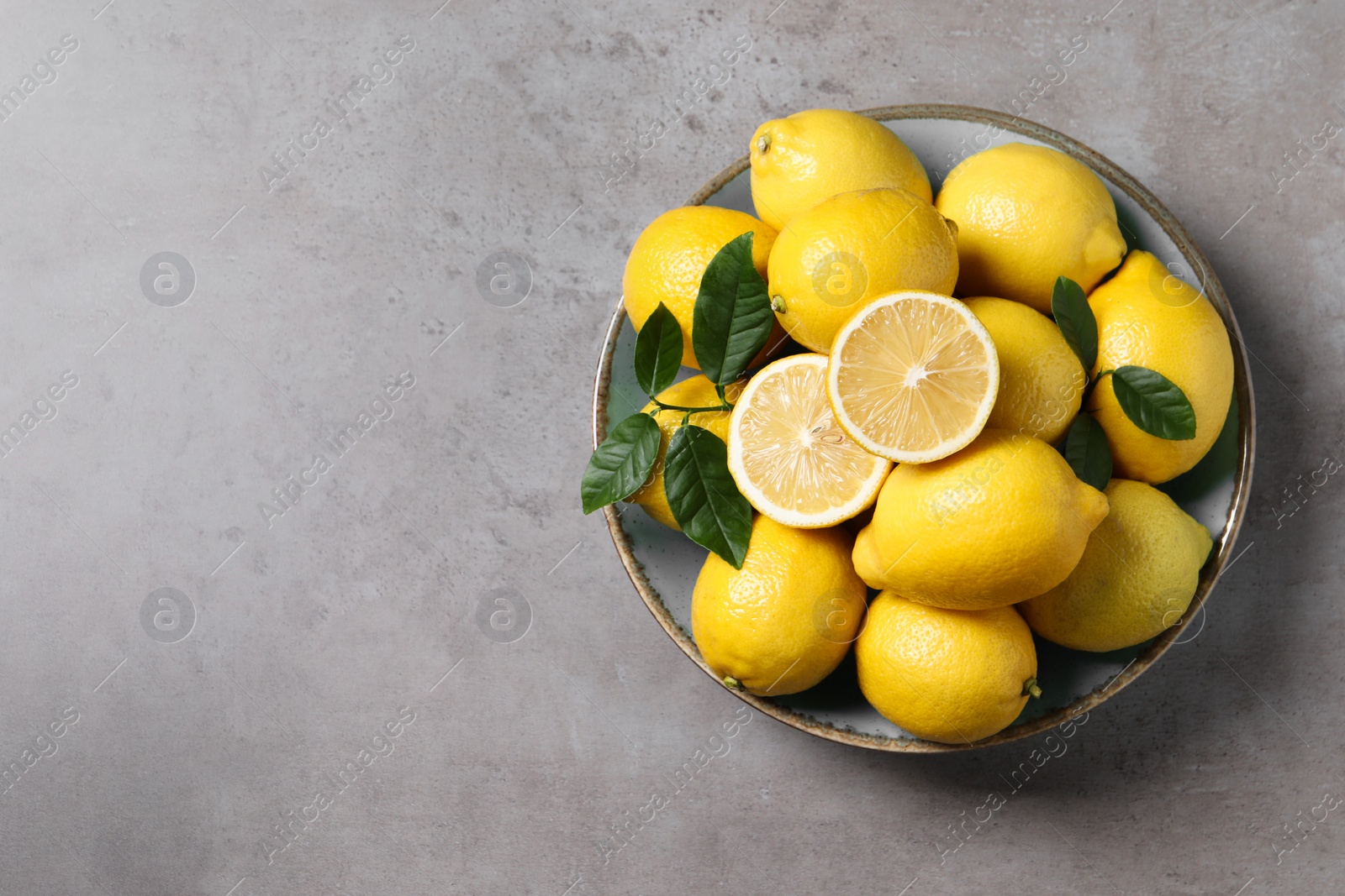 Photo of Fresh lemons and green leaves on grey table, top view. Space for text