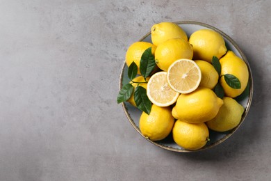 Fresh lemons and green leaves on grey table, top view. Space for text