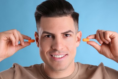 Photo of Man inserting foam ear plugs on light blue background