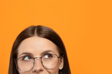 Photo of Woman in stylish eyeglasses on orange background, closeup. Space for text