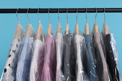 Photo of Dry-cleaning service. Many different clothes in plastic bags hanging on rack against light blue background