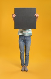 Photo of Woman holding black blank poster on yellow background. Mockup for design