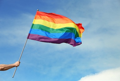 Photo of Gay man holding rainbow LGBT flag against blue sky