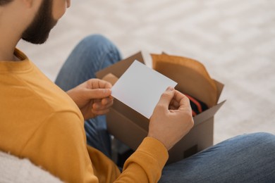 Photo of Man holding greeting card near parcel with Christmas gift, closeup