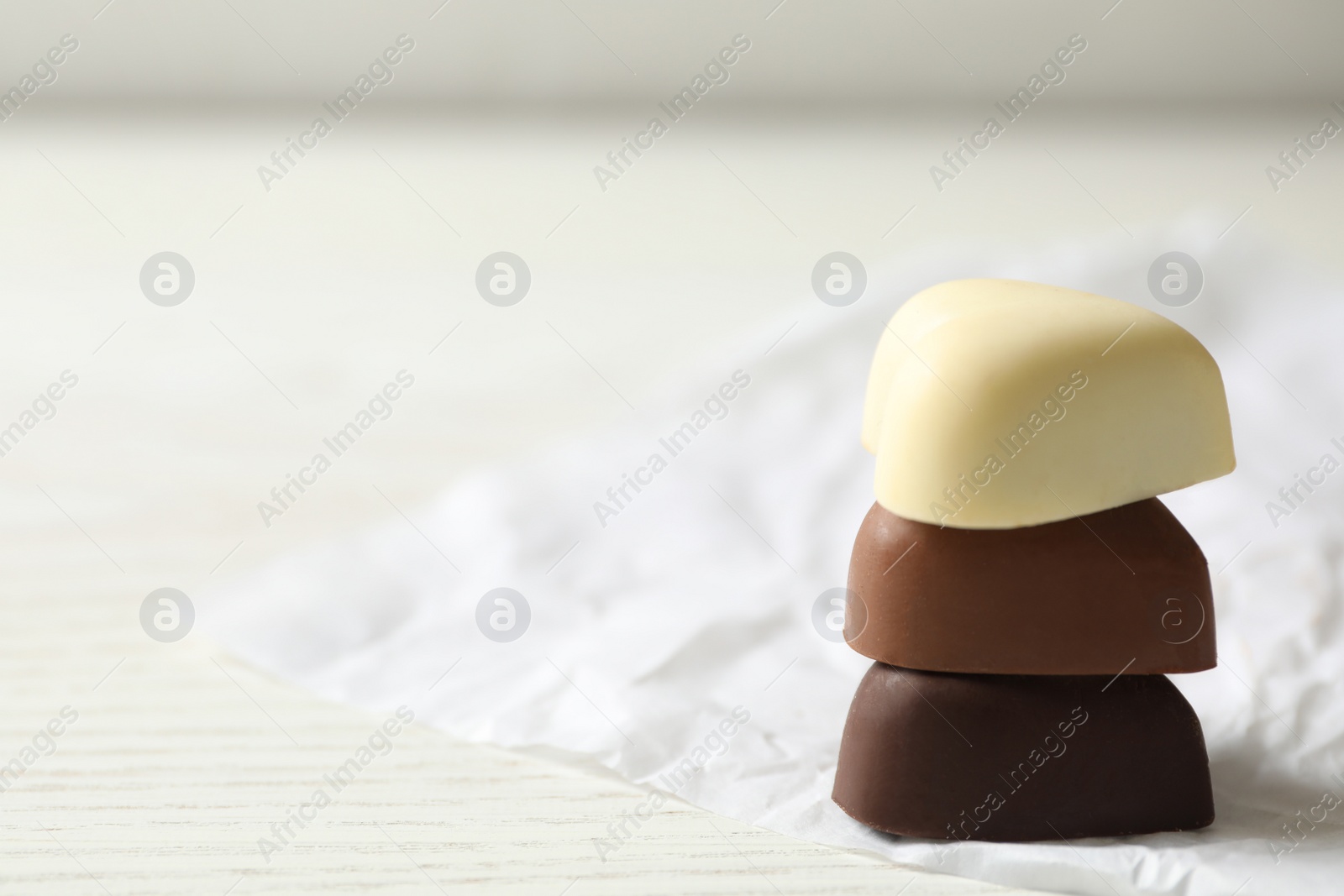 Photo of Beautiful heart shaped chocolate candies stacked on white wooden table, closeup. Space for text