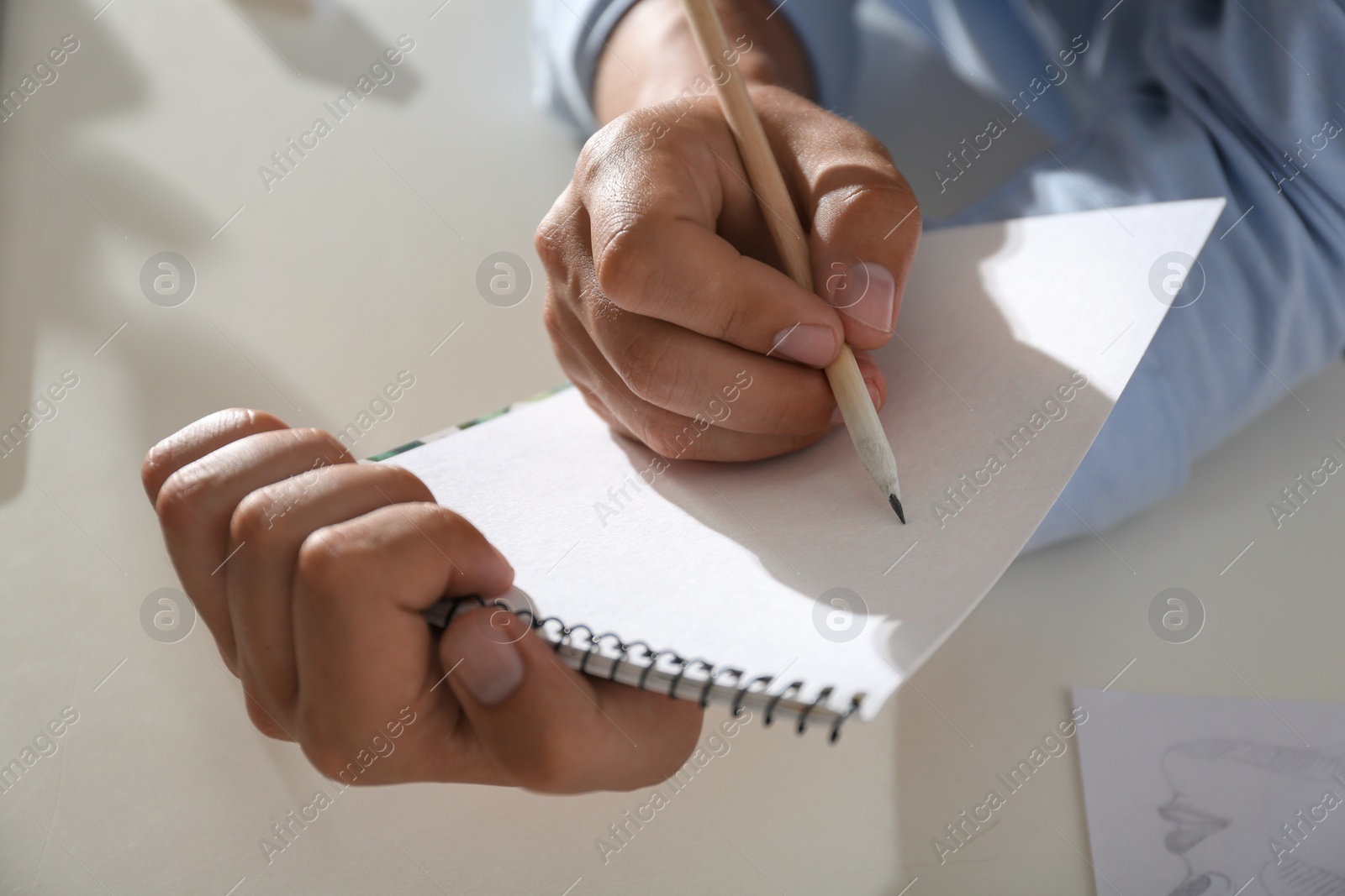 Photo of Man drawing with pencil in notepad at table, closeup