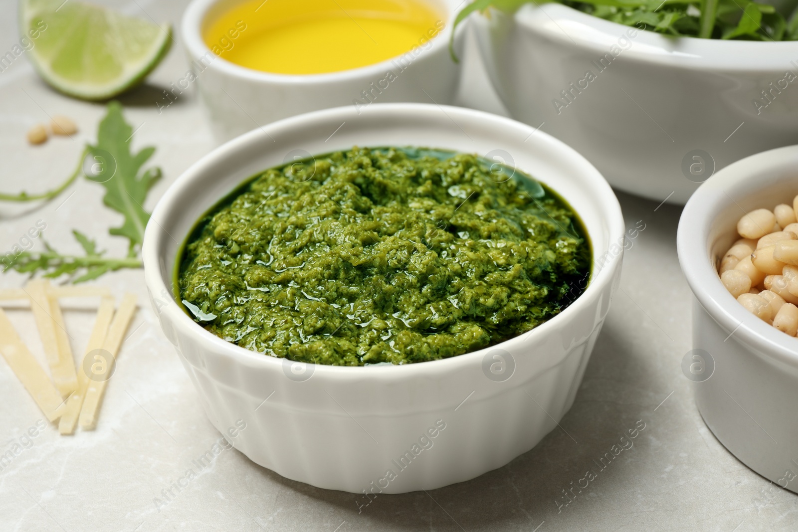 Photo of Bowl of tasty arugula pesto and ingredients on light table