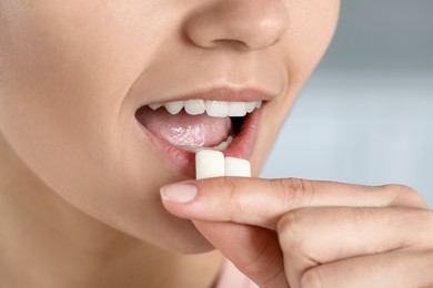 Photo of Woman putting chewing gums into mouth on blurred background, closeup