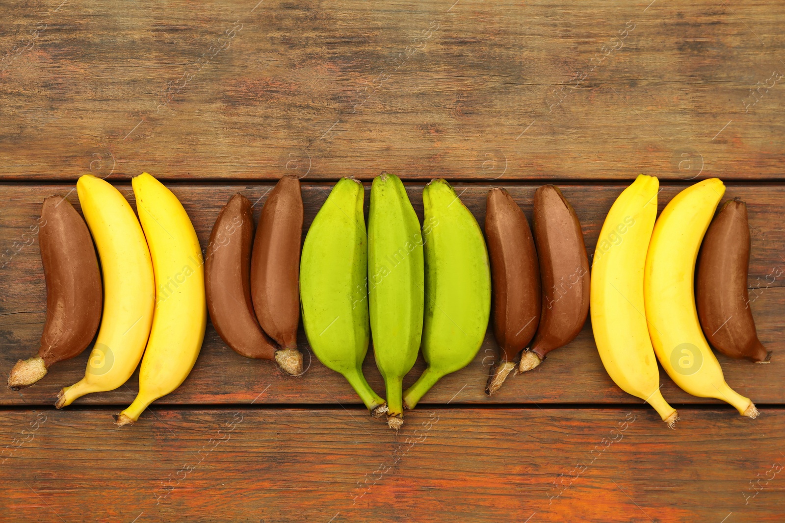 Photo of Many different bananas on wooden table, flat lay