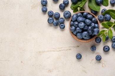 Photo of Tasty fresh blueberries and green leaves on light grey table, flat lay. Space for text