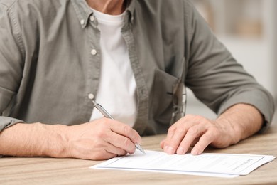 Photo of Senior man signing Last Will and Testament at wooden table, closeup