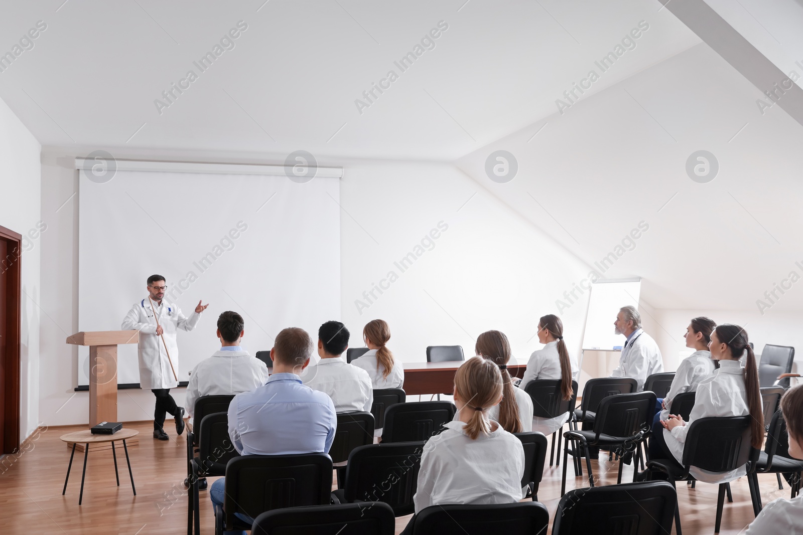 Photo of Doctor giving lecture in conference room with projection screen