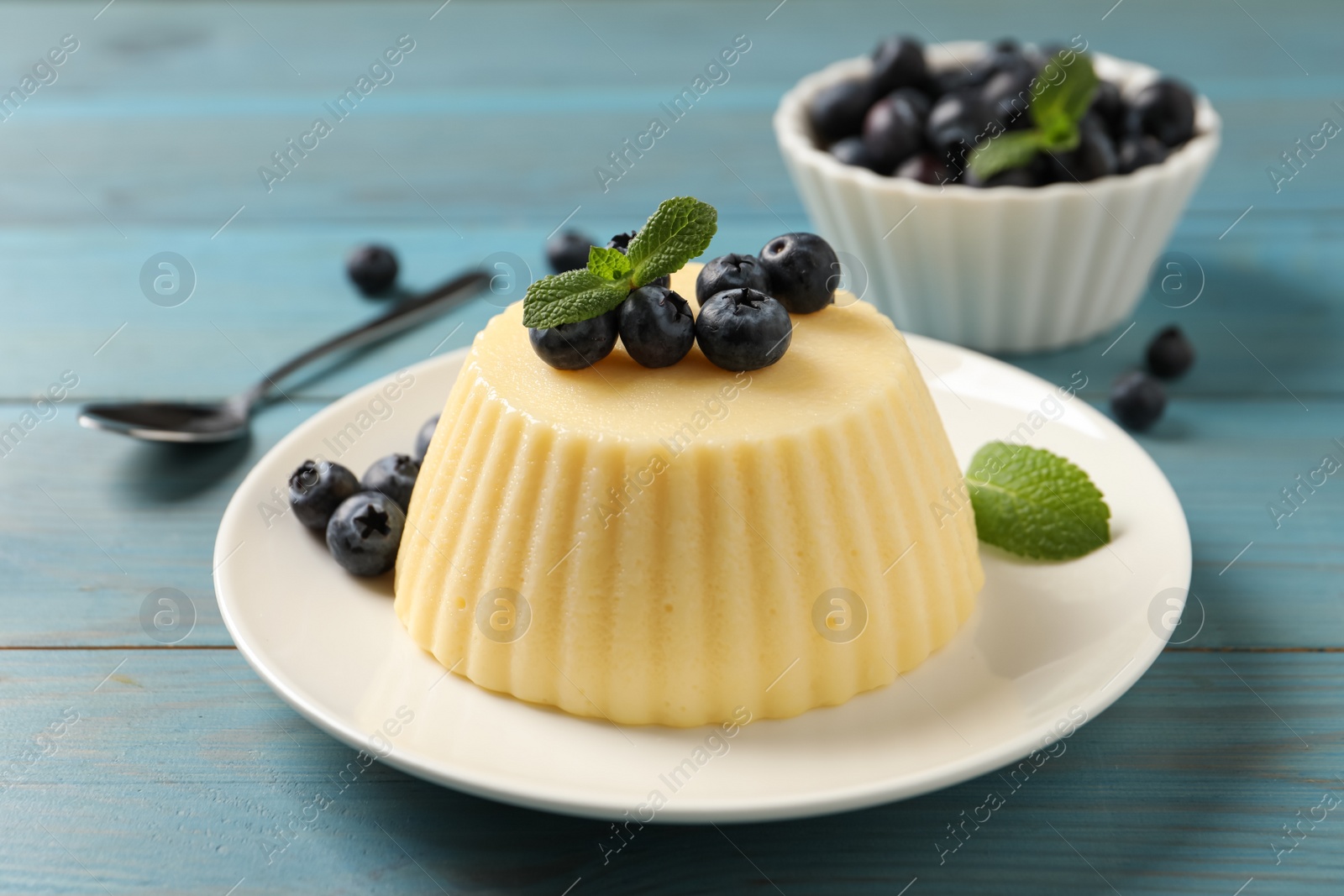 Photo of Delicious semolina pudding with blueberries on light blue wooden table