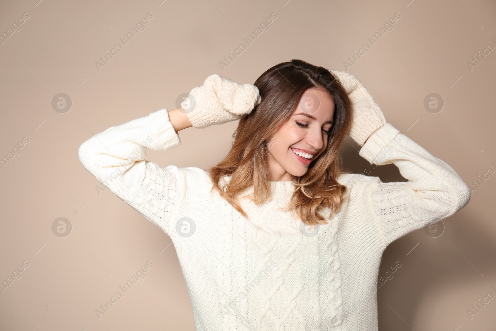 Image of Happy young woman wearing warm sweater and knitted mittens on beige background 