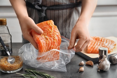 Photo of Woman putting marinated salmon fillet into plastic bag at table
