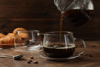 Pouring coffee into glass cup at wooden table, closeup